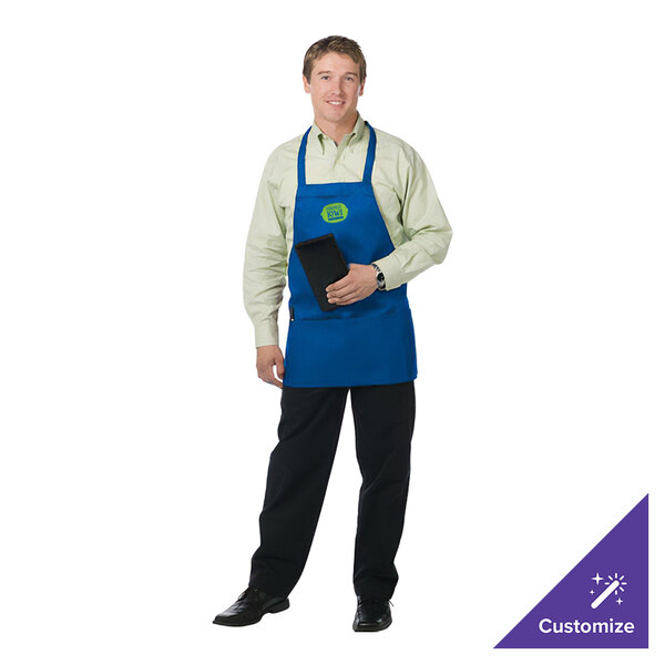 A man in a Chef Revival royal blue apron using a black phone in a professional kitchen.