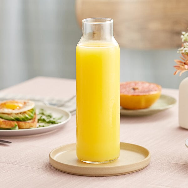 A Libbey glass bottle filled with orange juice on a table.