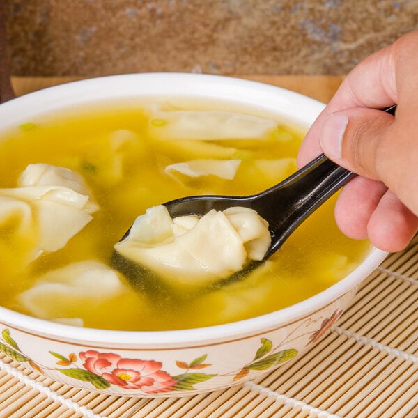 A hand holding a GET Black Melamine Soup Spoon over a bowl of soup.