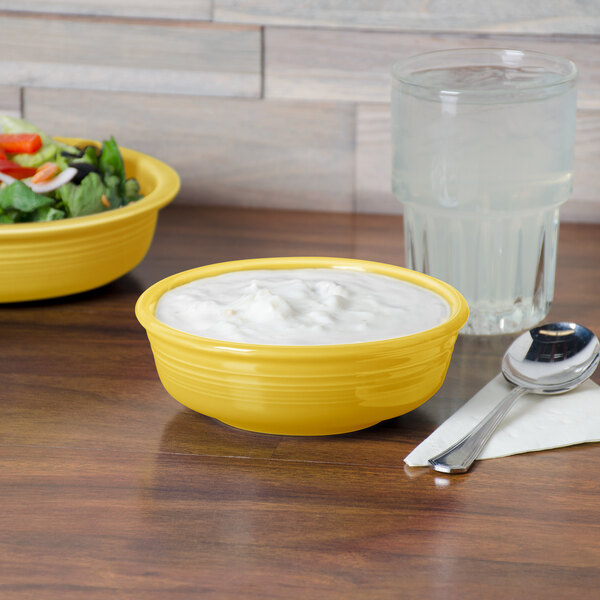 A yellow Fiesta china bowl with salad on a table.