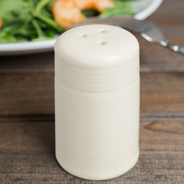 A Tuxton eggshell white pepper shaker on a table.