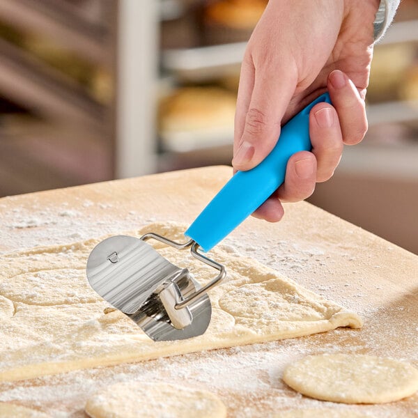 A stainless steel rolling circle cutter with a blue silicone handle being used to cut dough.