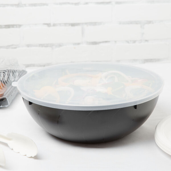 A Fineline clear plastic bowl with a flat lid filled with food on a table with spoons.