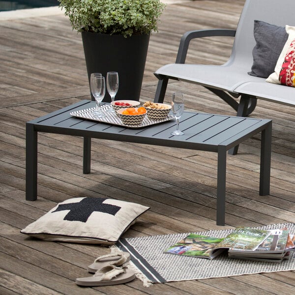 A Grosfillex Volcanic Black aluminum cocktail table on an outdoor patio with a glass of wine on it.