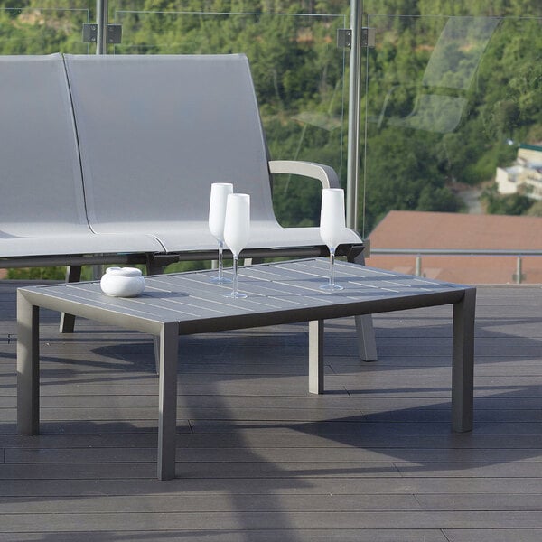 A Grosfillex aluminum cocktail table on an outdoor patio with wine glasses on it.