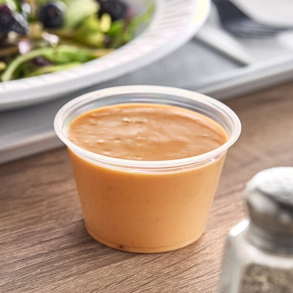 A plastic container of peanut butter next to a Dart plastic souffle cup of food.