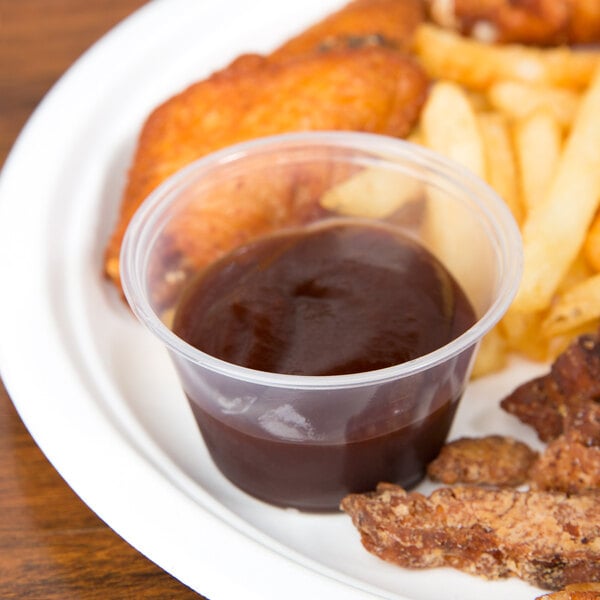 A plate of chicken wings and french fries with a plastic container of sauce.