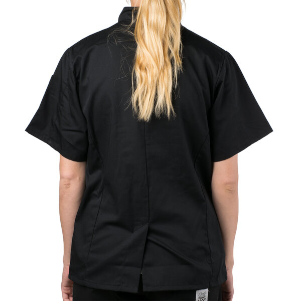 A woman wearing a Mercer Culinary black chef jacket with cloth knot buttons.
