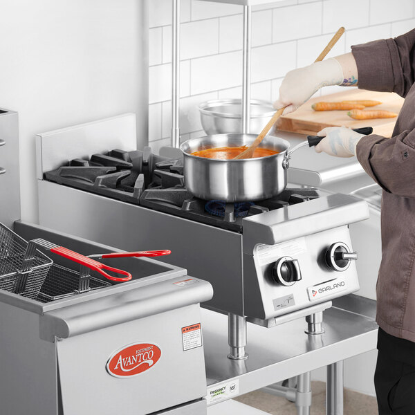 A chef using a Garland countertop range to cook in a metal pot.