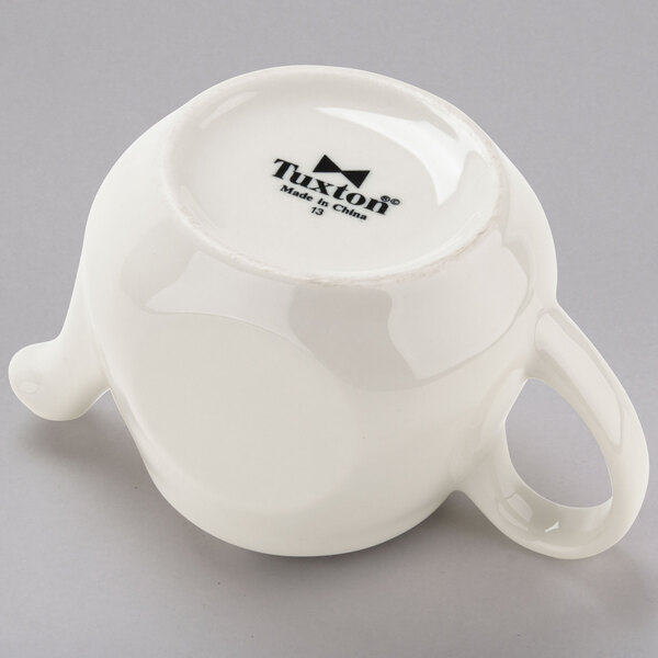 An eggshell white china teapot with a black handle.