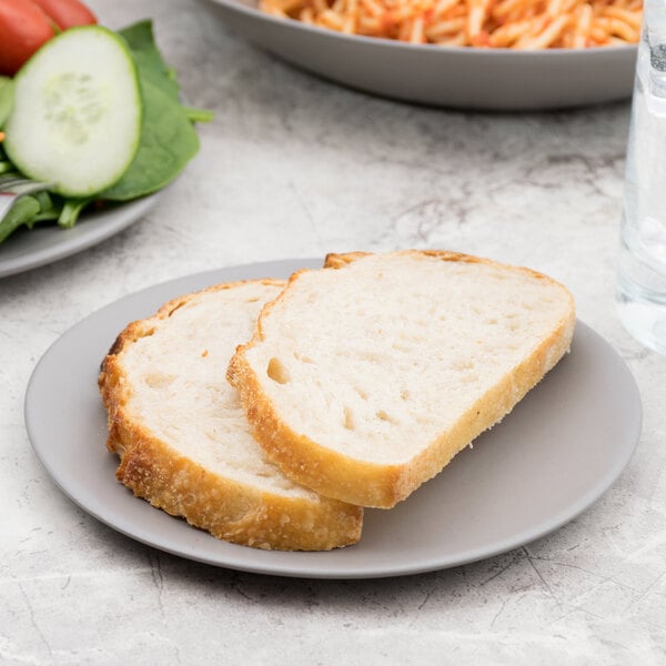 A piece of bread on a 10 Strawberry Street matte gray stoneware plate on a table.