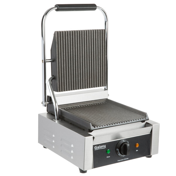 A Galaxy stainless steel Panini grill with grooved plates on a table.