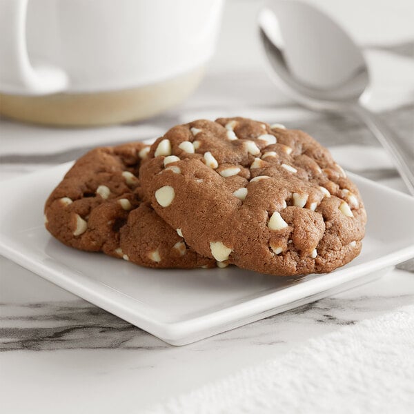 A plate of chocolate chip cookies with Ghirardelli white chocolate chips and a white cup.