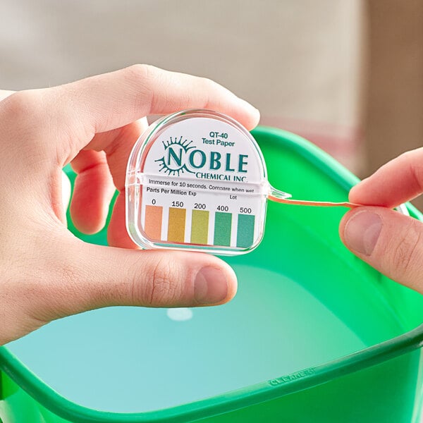 A hand holding a plastic container of Noble Chemical Quaternary Test Papers.