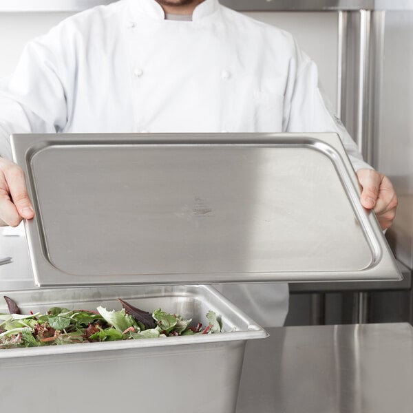 A chef using a Vollrath stainless steel pan cover on a tray of salad.