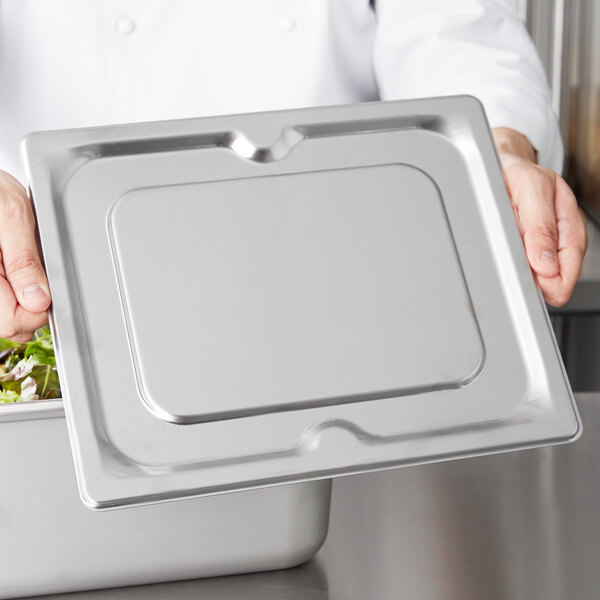 A chef holding a Vollrath stainless steel 1/2 size steam table pan cover.