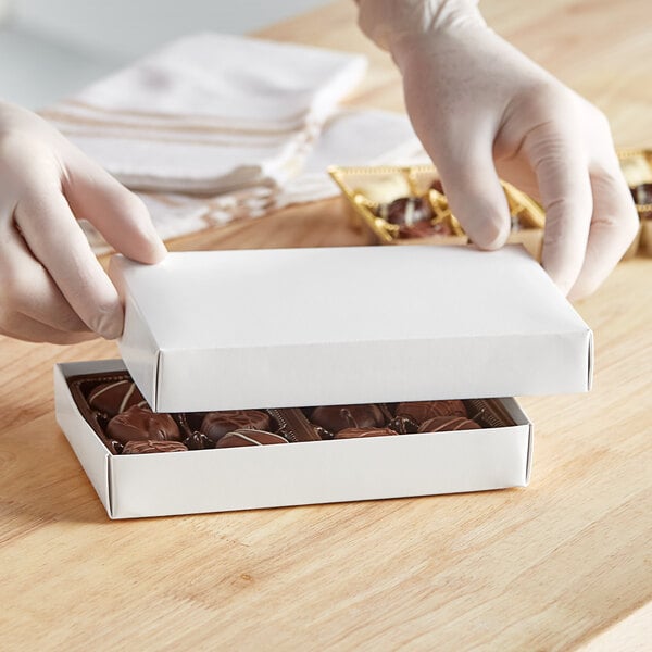 A gloved hand opens a white 1/2 lb. candy box to reveal chocolates.