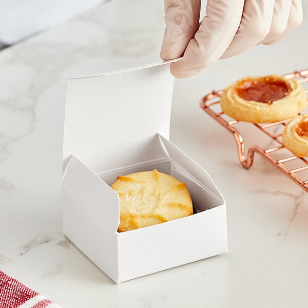 A hand holding a small white candy box filled with food.