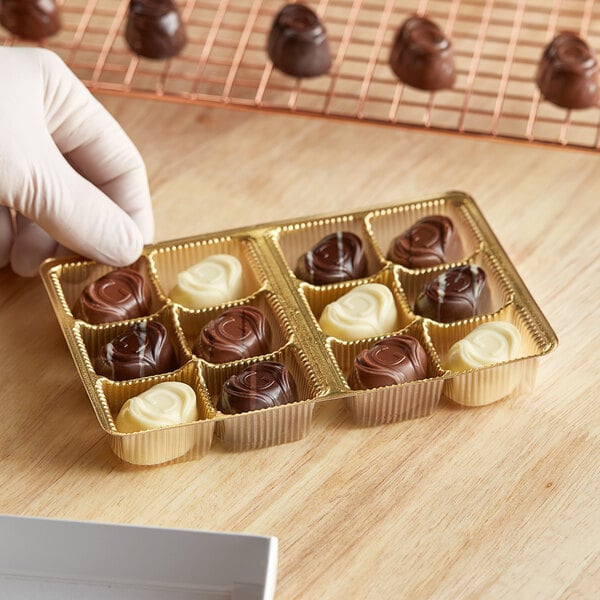 A gloved hand holding a gold 12-cavity candy tray filled with chocolates.