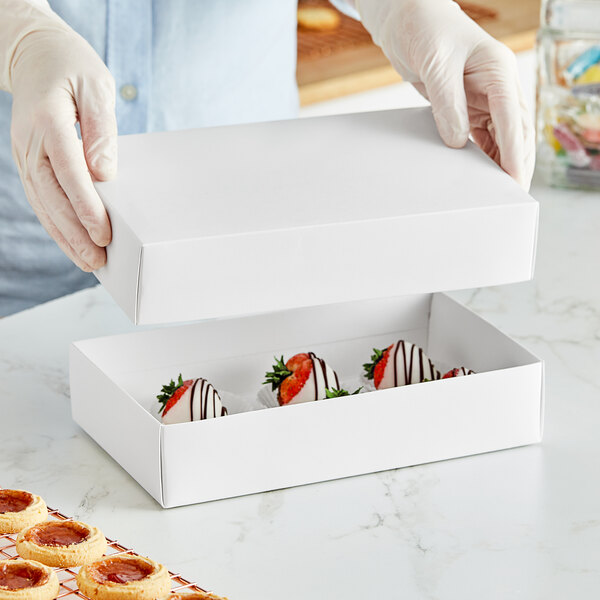 A person in gloves holding a white candy box with strawberries in it.
