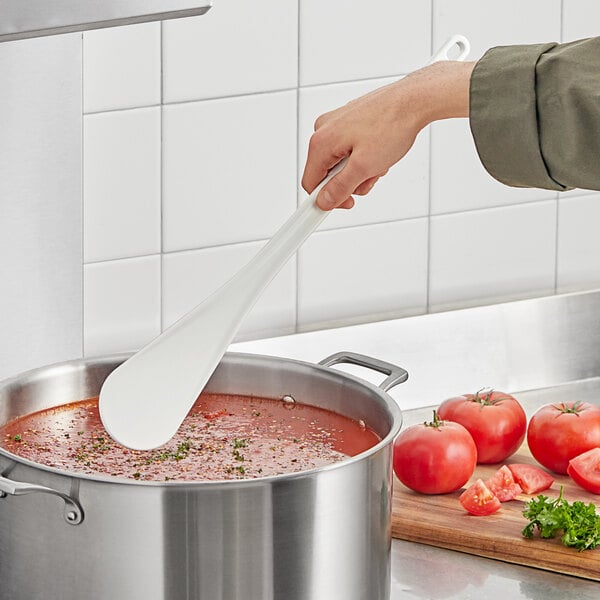 A person stirring a pot of tomato soup with a white high temperature spootensil.