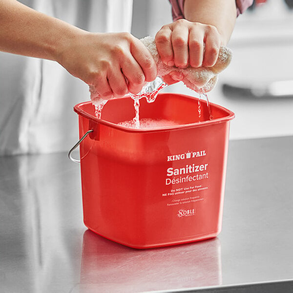 hands squeezing water out of a kitchen towel in a red sanitizing pail