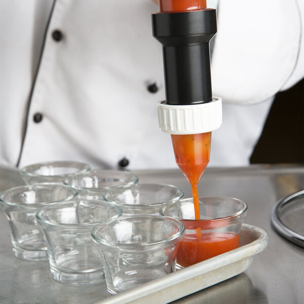 A chef using a Matfer Bourgeat portion control funnel to pour sauce into small glasses.
