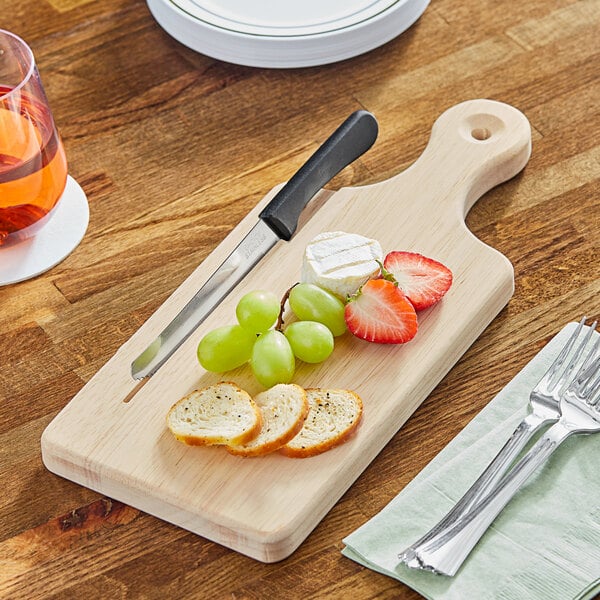 A Choice wooden serving / cutting board with fruit and cheese and a knife on it.