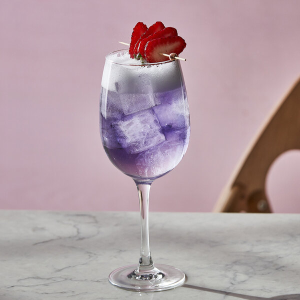 A close-up of an Arcoroc Excalibur Breeze wine glass filled with purple liquid and strawberries.
