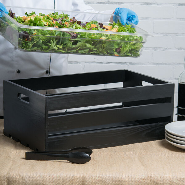 A person holding a salad in an American Metalcraft black wood crate.