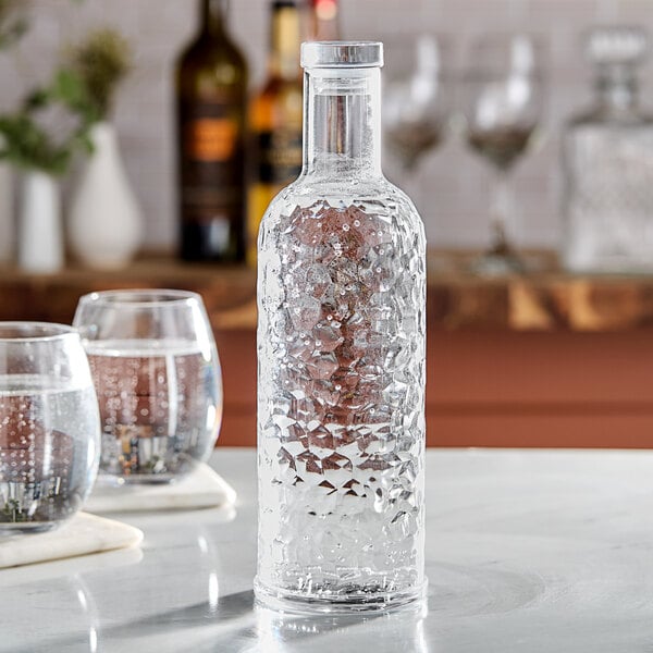 An American Metalcraft pebbled plastic water bottle on a table with a glass of ice water.