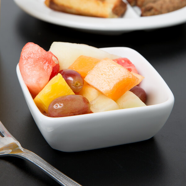 A Libbey square white porcelain bowl filled with fruit with a fork next to it.