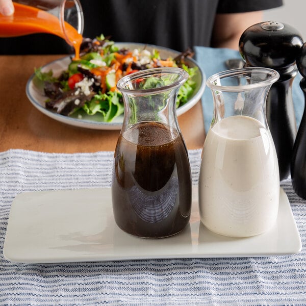 A person pouring Hidden Valley Ranch dressing into glass containers on a plate of salad.