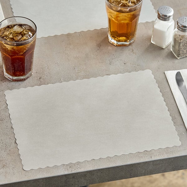 A gray Choice paper placemat with a scalloped edge on a table with a glass of brown liquid and ice.