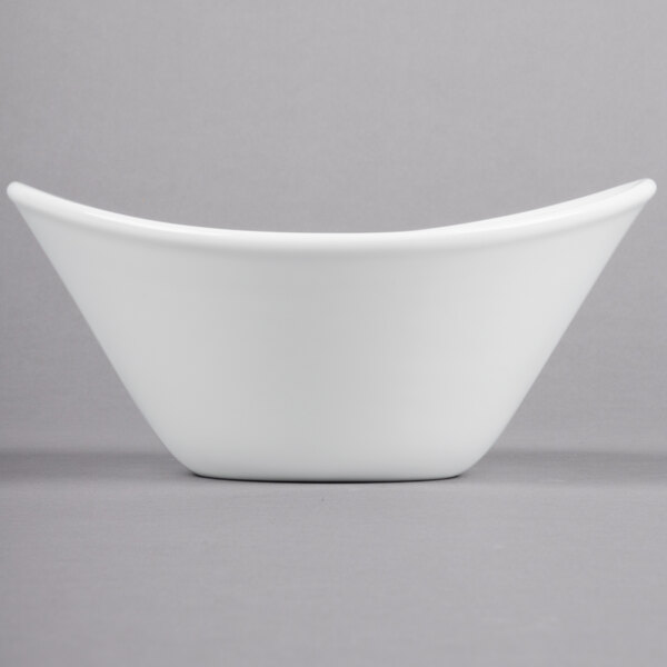 A close-up of a Libbey Aluma White Porcelain Infinity Bowl with a curved edge on a gray surface.