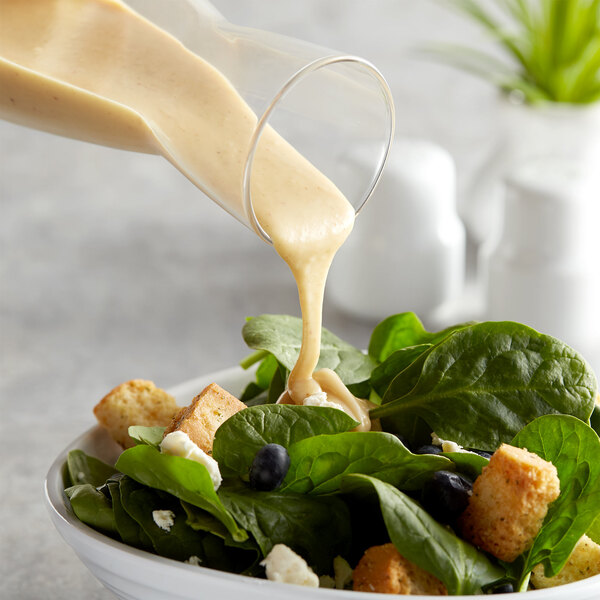 A salad with spinach, blueberries, and croutons in a glass bowl with Hidden Valley Golden Honey Mustard dressing being poured over it.