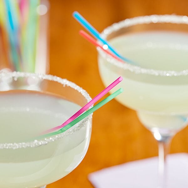 Two glasses of colorful drinks with neon straws on a table.