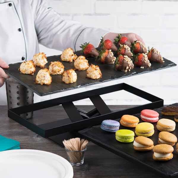 A chef holding an Elite Global Solutions black slate melamine serving board with pastries.