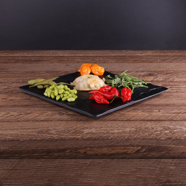 An Elite Global Solutions faux black slate melamine serving board with vegetables on a wood table.