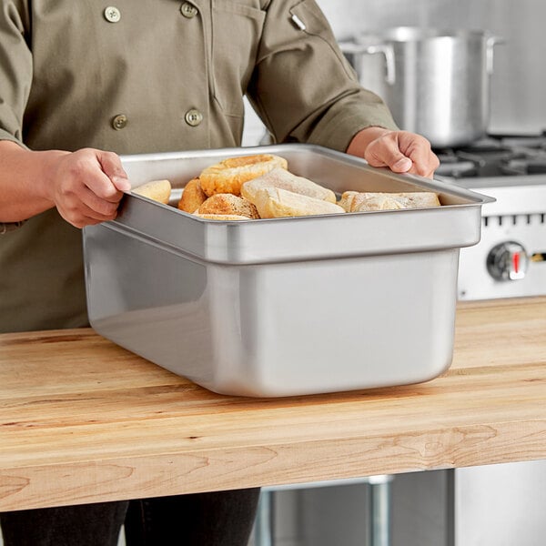 A woman holding a Vollrath stainless steel pan full of food.