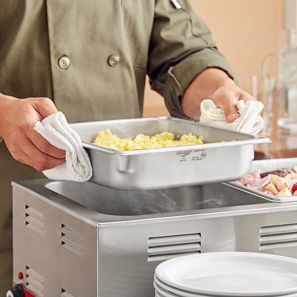 A man in a chef's uniform using a Vollrath Super Pan to prepare food on a hotel buffet counter.