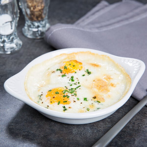 A white Tuxton round china dish with shirred eggs and herbs on top.