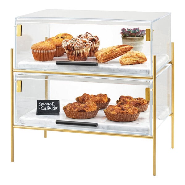 A two-tiered clear pastry case with a brass frame, displaying assorted baked goods.