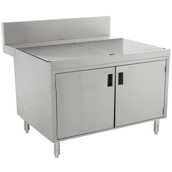 A stainless steel Advance Tabco enclosed drainboard cabinet with doors and shelf.