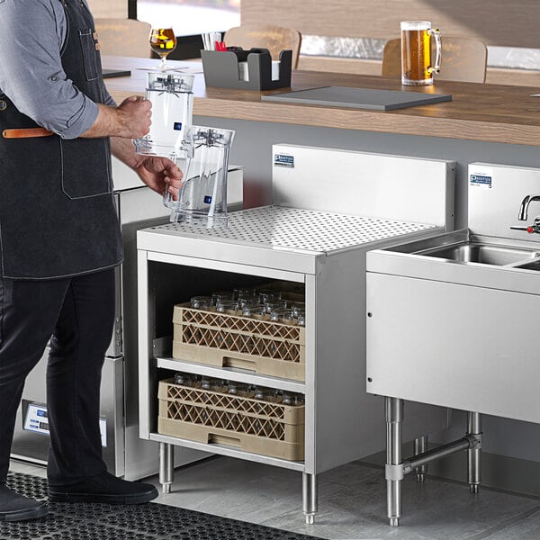 A man using an Advance Tabco stainless steel drainboard shelf next to a sink in a professional kitchen.