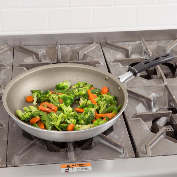 A Vollrath Wear-Ever aluminum non-stick fry pan with vegetables cooking in it on a stove.