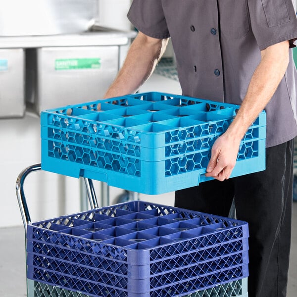 A blue Carlisle OptiClean 16 compartment glass rack with 2 extenders being handled in a commercial kitchen setting.