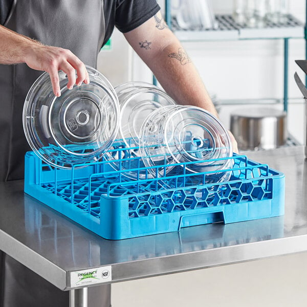 A man in an apron putting clear plates in a Carlisle dish rack on a counter in a professional kitchen.