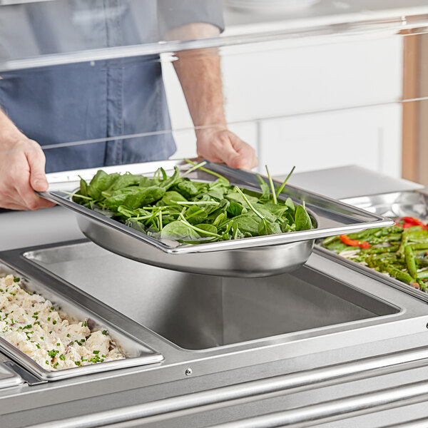 A person using a Vollrath stainless steel oval pan to serve food on a buffet counter.