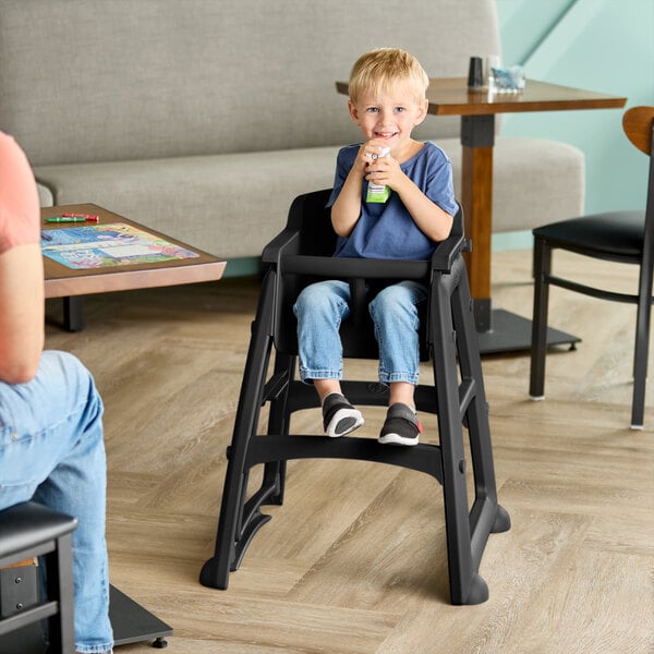 A black Rubbermaid restaurant high chair without wheels, shown assembled and in use by a child.